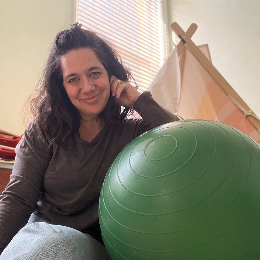 Dr. Sarah Muir smiling beside a green therapy ball, with a child's play tent behind her